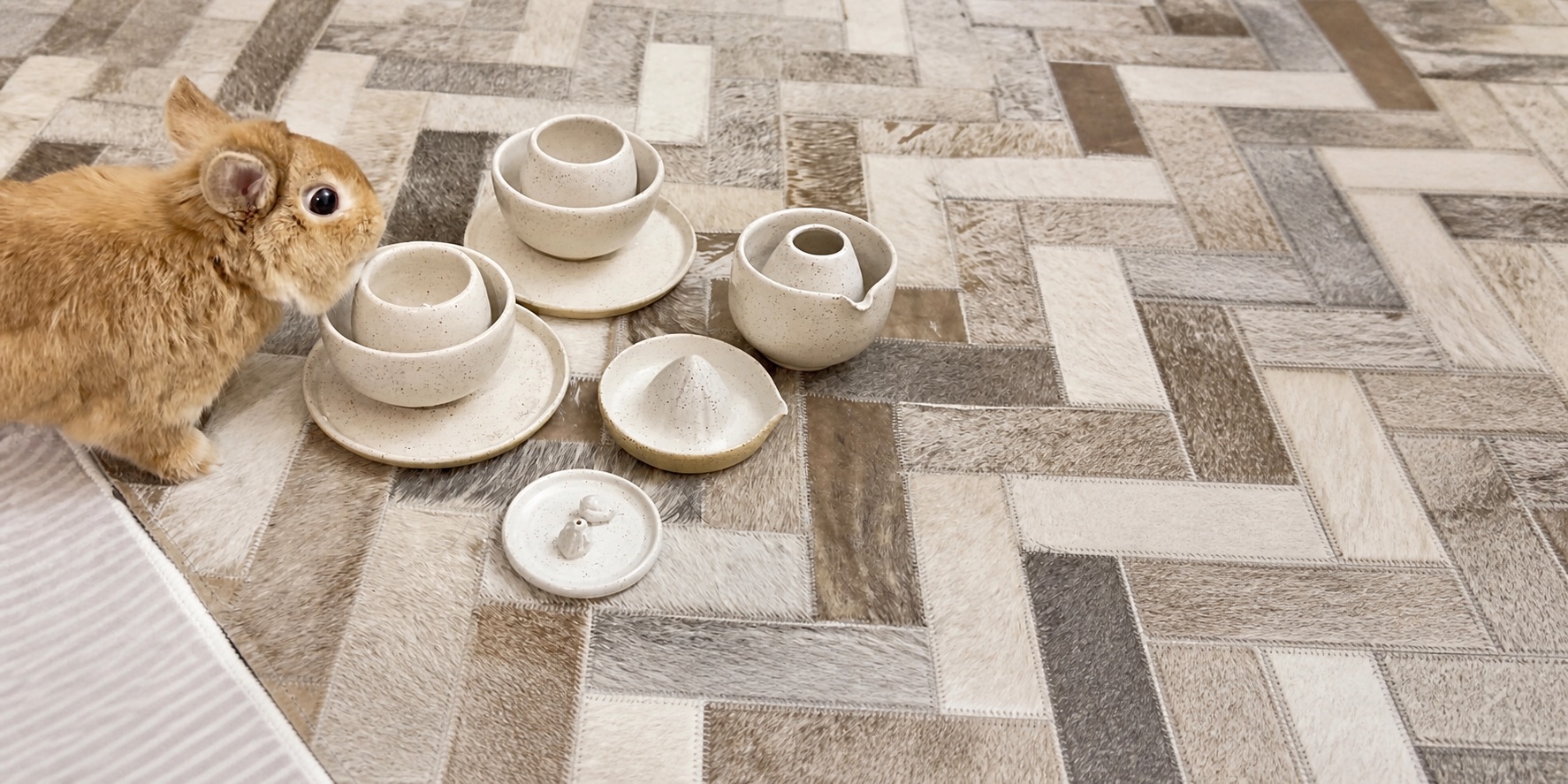 Puppy, a brown rabbit, beside a collection of handmade speckled ceramic bowls and dishes.
